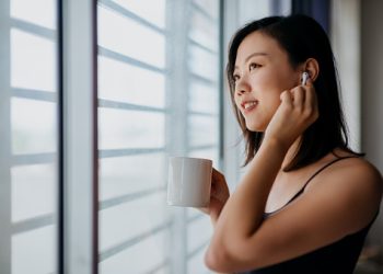 Young asian woman listening to music with wireless headphone and drinking coffee, enjoying a peaceful moment at home